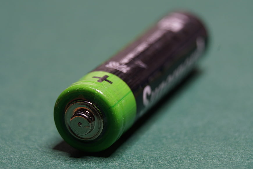 Close-up of green and black AA battery on teal background