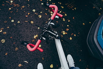 Top-down view of bicycle handlebars with red tape on autumn road