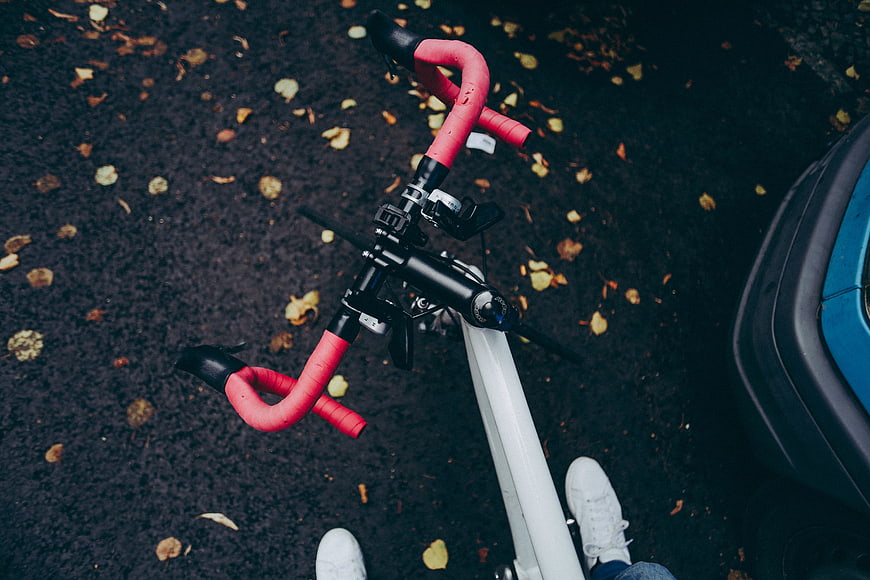 Top-down view of bicycle handlebars with red tape on autumn road