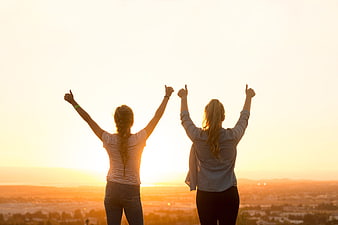 Two women celebrating with thumbs up at sunset