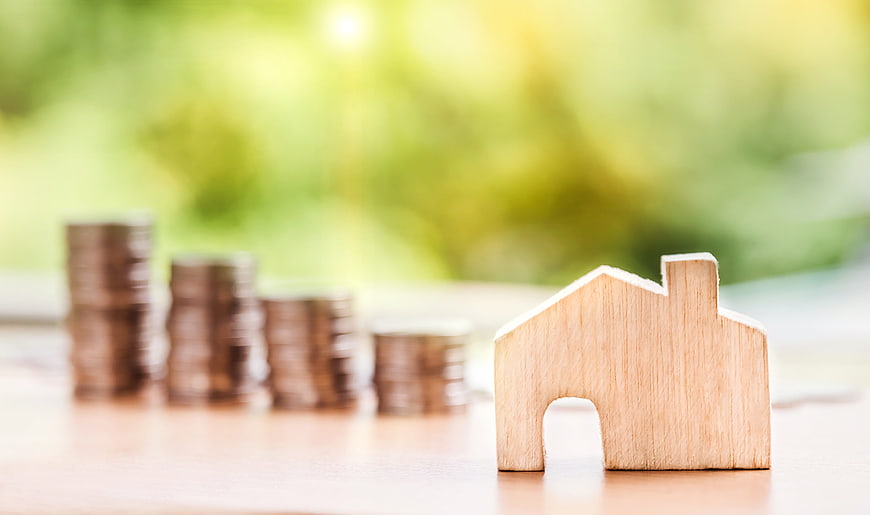 Wooden house model with stacks of coins for real estate investment