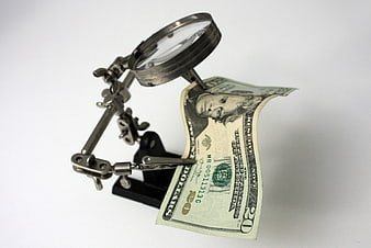 Magnifying glass inspecting twenty dollar bill on white background