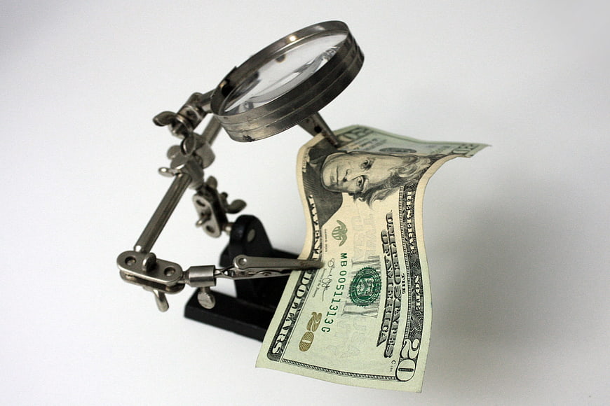 Magnifying glass inspecting twenty dollar bill on white background