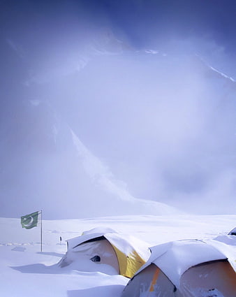Snow-covered tents and Pakistani flag in winter mountain landscape
