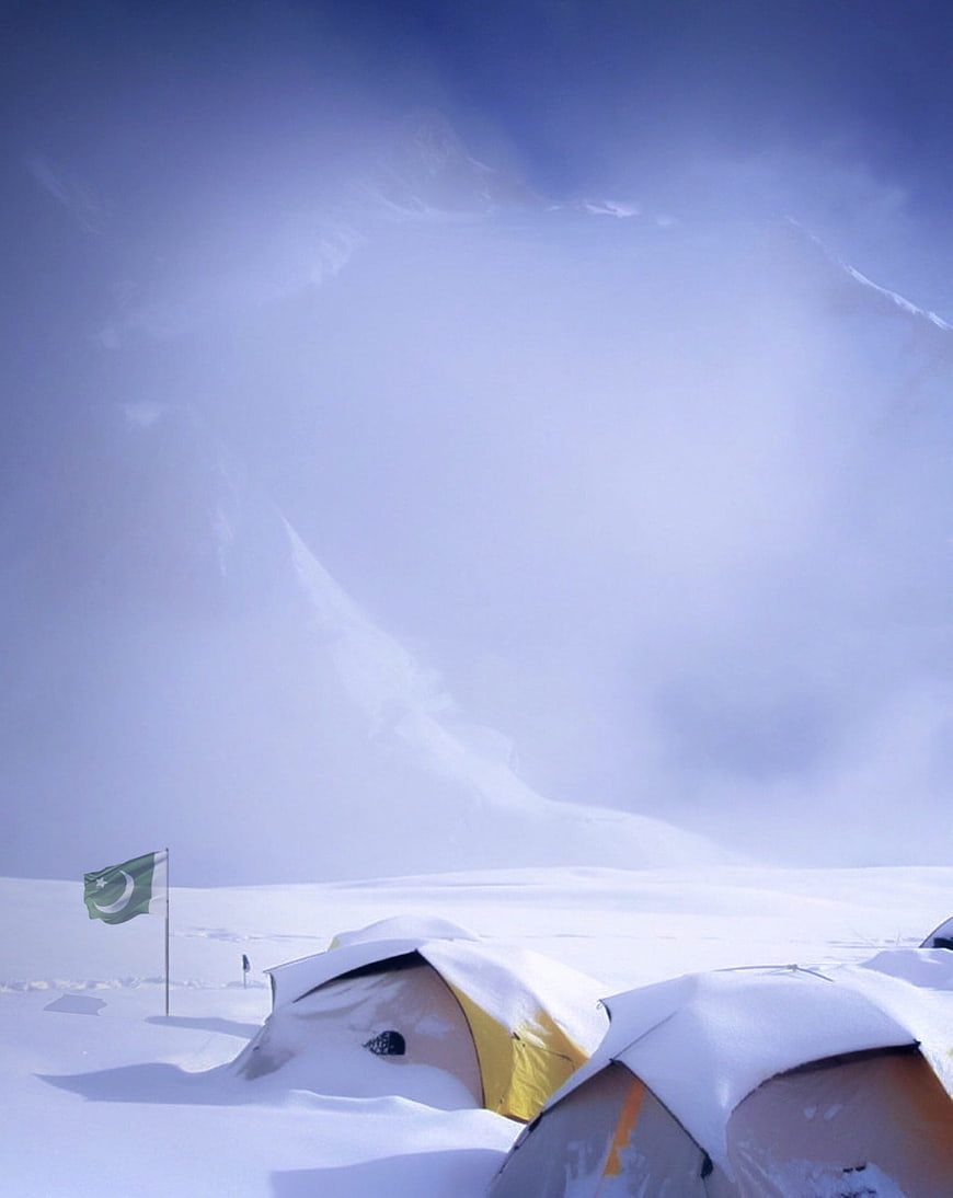 Snow-covered tents and Pakistani flag in winter mountain landscape