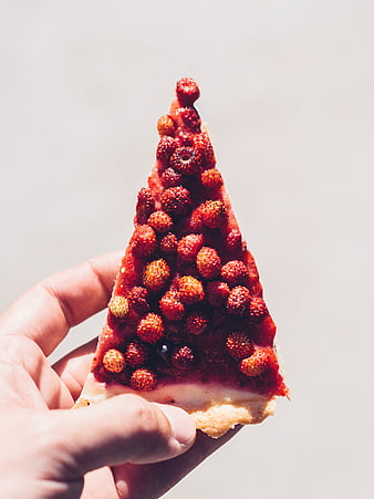 Hand holding strawberry tart slice against white background