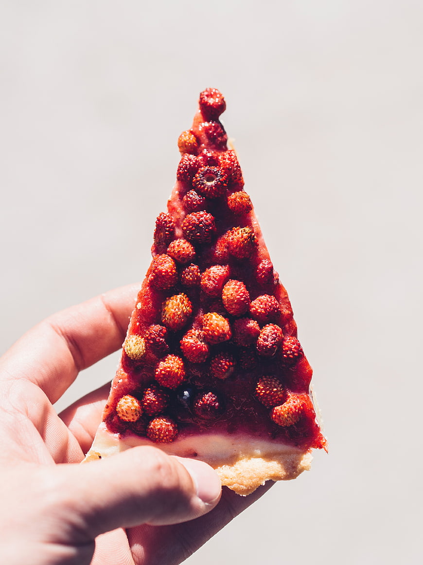 Hand holding strawberry tart slice against white background
