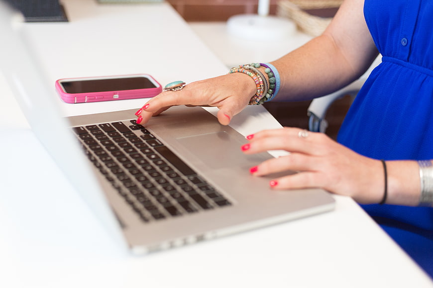 Woman Typing on Laptop with Smartphone on Desk