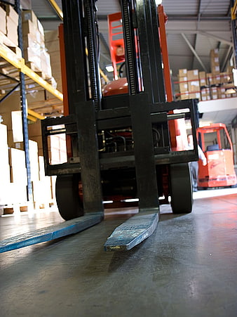 Low angle view of forklift forks in a busy warehouse aisle