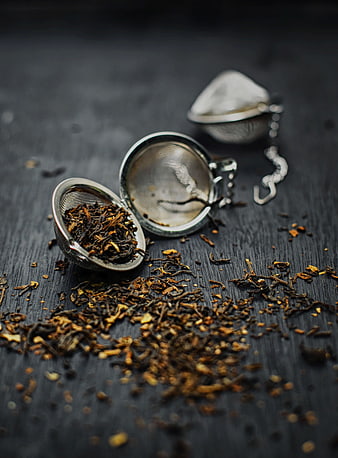 Loose leaf tea spilling from metal infuser on dark wood
