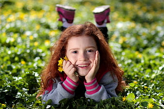 Happy Redhead Girl Lying in Clover Field with Yellow Flowers