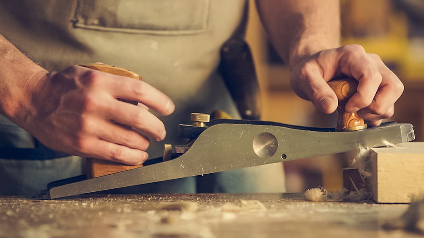 Carpenter using hand plane on wood block