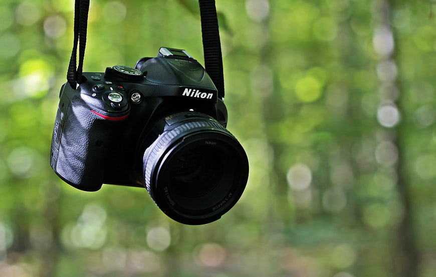 Nikon DSLR camera hanging against a blurred green forest background