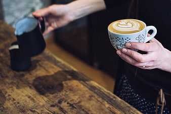 Barista holding latte art coffee cup on wooden counter