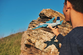 Man holding blue remote control airplane on rocky hill