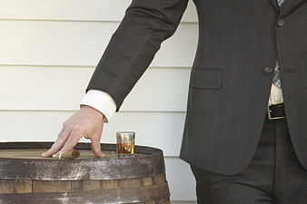 Man in Suit Reaching for Whiskey and Cigar on Barrel