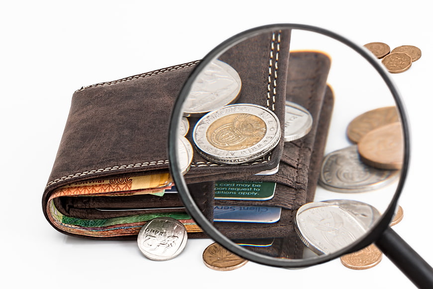 Magnifying glass inspecting coins in a leather wallet