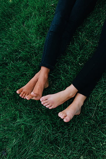 Barefoot friends sitting on green grass in black jeans