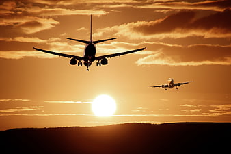 Two Airplanes Flying Silhouetted Against Golden Sunset Sky