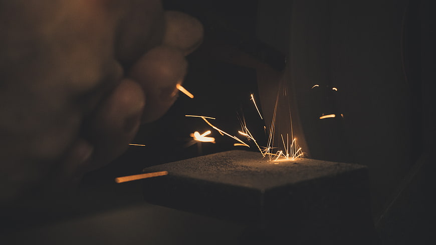 Close-up of hand striking flint to create sparks in dark