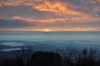 Dramatic sunset over misty mountain landscape with silhouetted trees