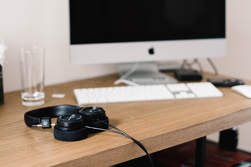 Black Headphones on Wooden Desk with Blurred Computer Background