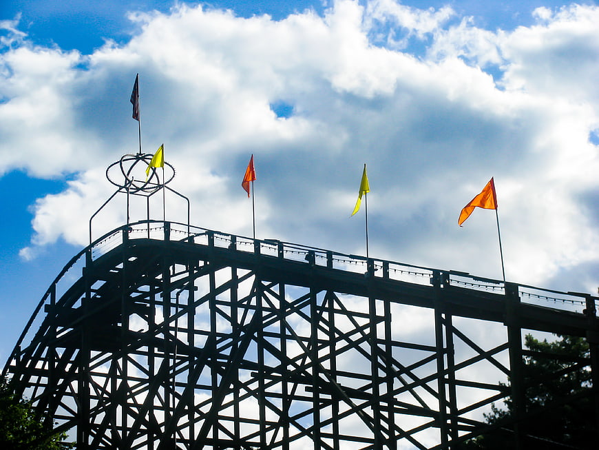 Silhouette of wooden roller coaster with flags against blue sky
