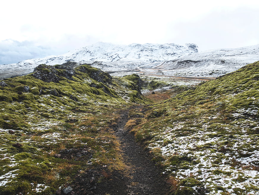 Snowy hiking trail through green mossy highlands