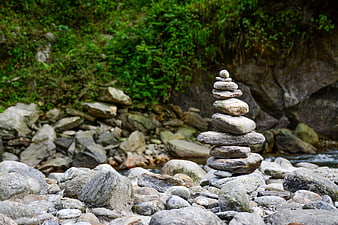 Balanced stone cairn stack on riverbank with green foliage