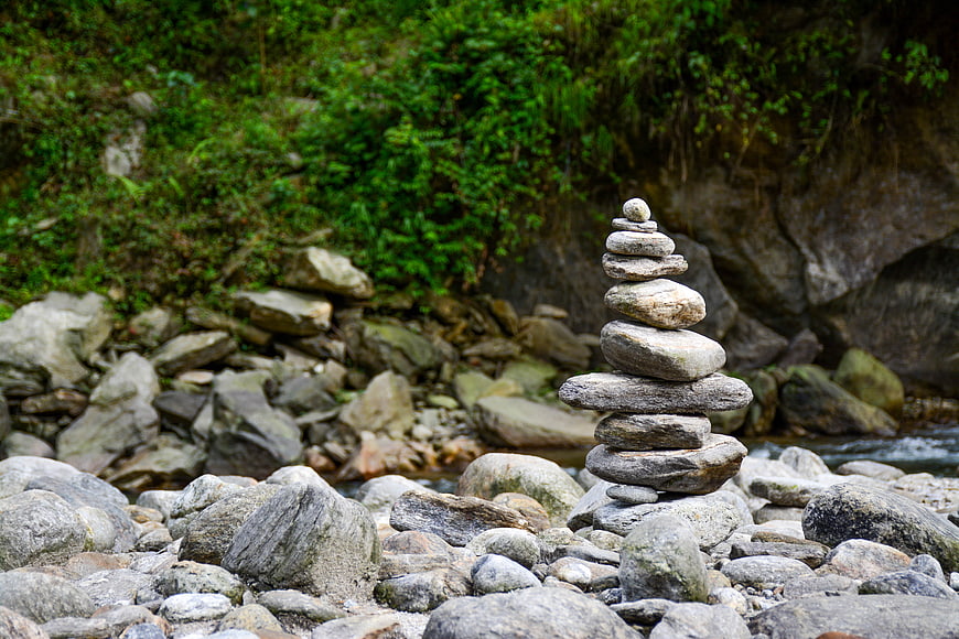 Balanced stone cairn stack on riverbank with green foliage