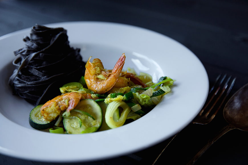 Black squid ink pasta with shrimp and zucchini on white plate