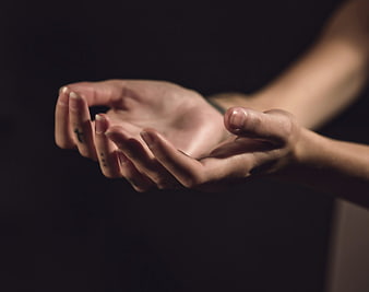 Close-up of cupped hands with cross tattoo on dark background