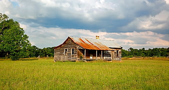 Old Rustic Wooden House in Green Field with Cloudy Sky