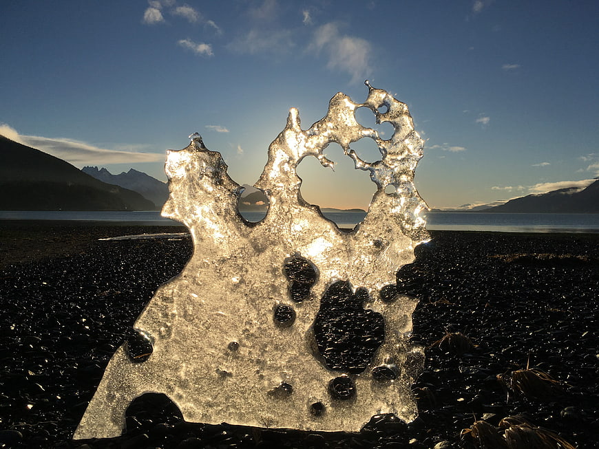 Translucent ice sculpture on black sand beach at sunset