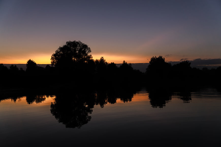 Silhouette of trees reflecting in calm lake at sunset
