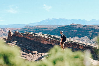 Man hiking on red rock ridge overlooking vast canyon landscape