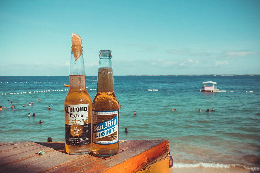 Corona and San Miguel beer bottles on beach railing