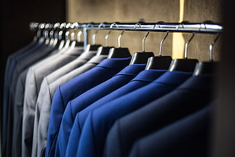 Row of blue and gray suits on hangers in a closet