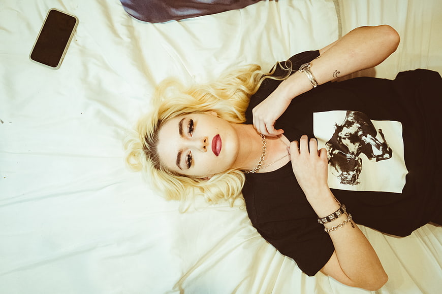 Blonde woman lying on bed looking up at camera