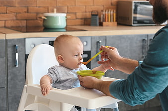 Father Feeding Baby in High Chair in Modern Kitchen