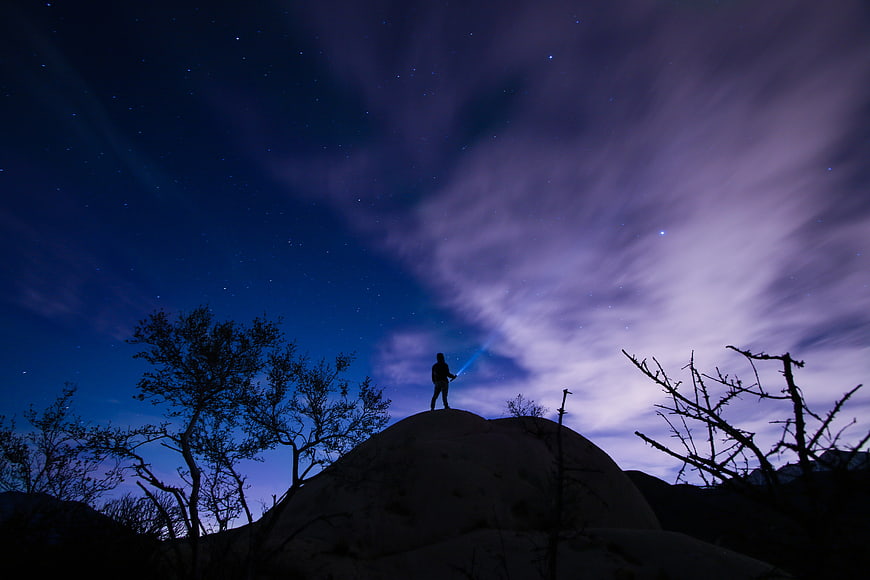 Silhouette of Man with Flashlight on Hill Under Starry Night Sky