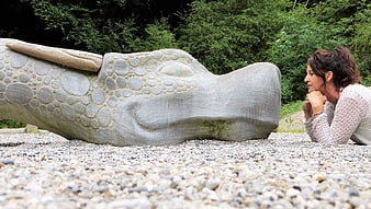 Woman lying on gravel gazing at large stone dragon sculpture