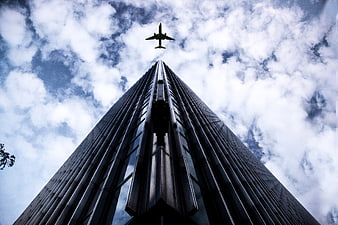 Low angle view of skyscraper with airplane flying overhead