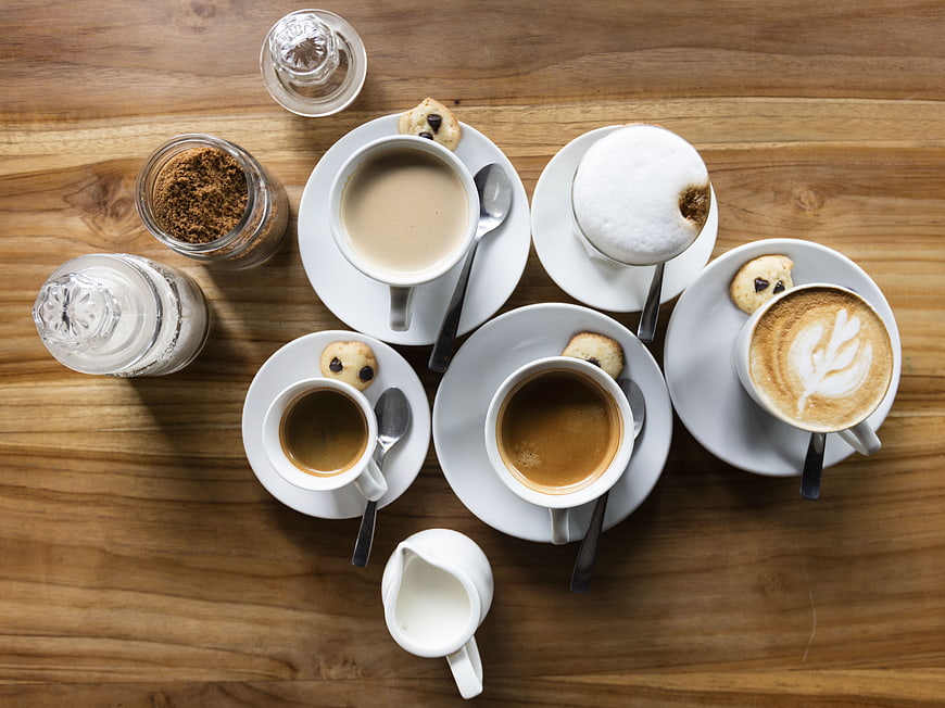 Overhead view of assorted coffee cups and cookies on wooden table