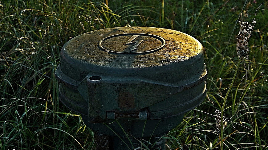 Rusty green electrical box with lightning bolt symbol in tall grass
