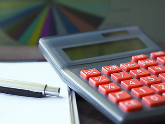 Close-up of calculator and pen on desk with financial charts