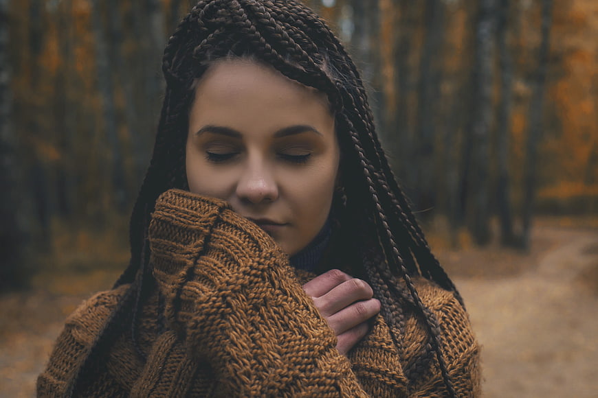 Woman with braids in cozy sweater in autumn forest