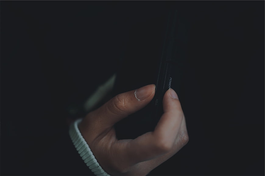 Close-up of hand holding black remote control in dark setting
