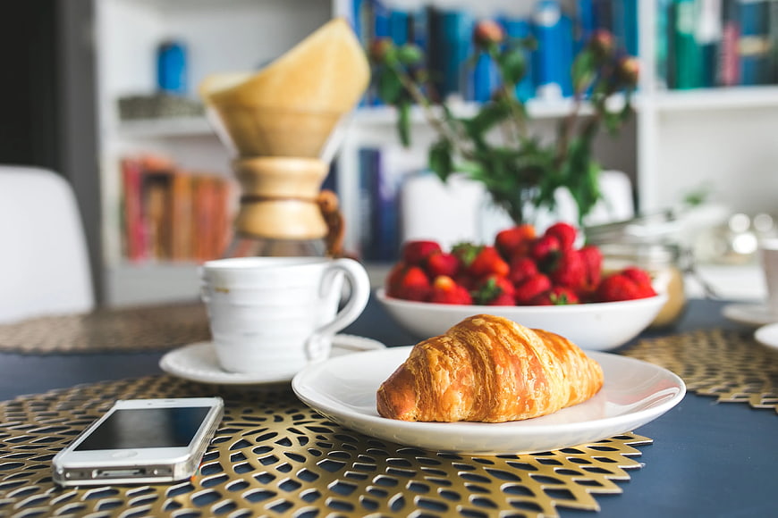 Fresh croissant and strawberries breakfast with coffee and smartphone