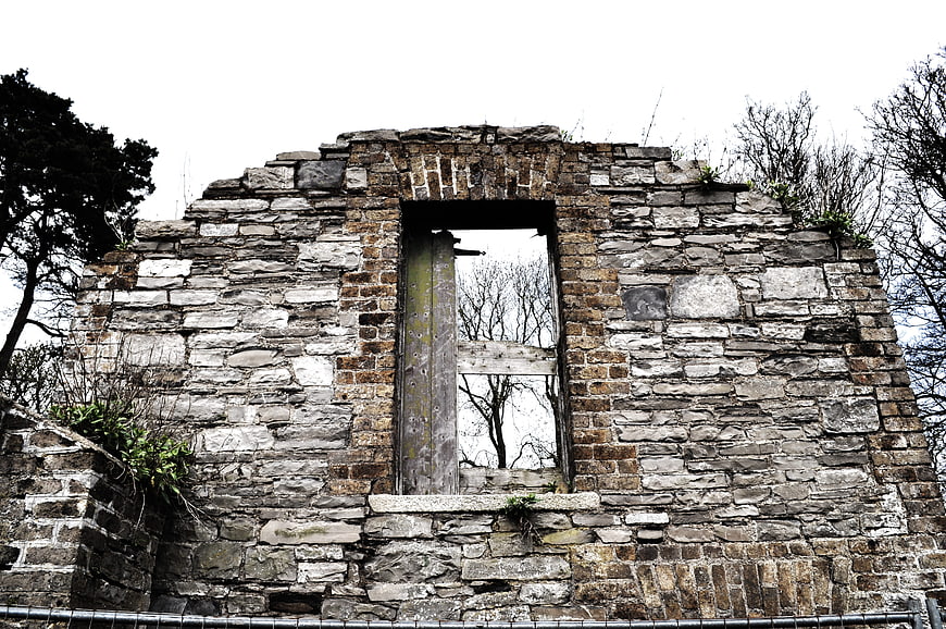 Weathered stone ruins with empty window frame and overgrown vegetation